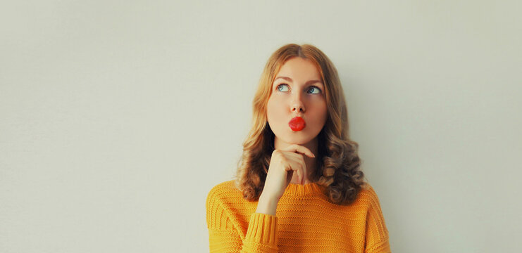 Portrait of beautiful wondering young woman thinks looks up, female caucasian model 20s blowing her lips with red lipstick wearing yellow sweater on white background, blank copy space