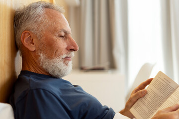 Fototapeta premium Closeup, handsome, serious senior man reading book, lying in bed, morning routine