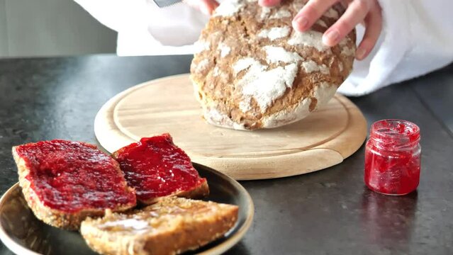 sliced bread.Woman in white bathrobe cut a crispy bread close-up. Fresh bread with jam and honey for breakfast. 4k footage