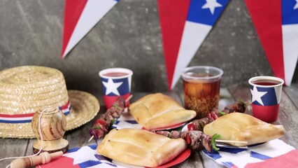 Fiestas Patrias Chile September 18, Independence Day. Empanadas, Anticuchos, mote con huesillo, chicha or wine, Sombrero, huaso, chupallas, straw and emboque, on a wooden table with flag and balloons