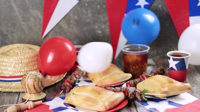 Fiestas Patrias Chile September 18, Independence Day. Empanadas, Anticuchos, mote con huesillo, chicha or wine, Sombrero, huaso, chupallas, straw and emboque, on a wooden table with flag and  balloons