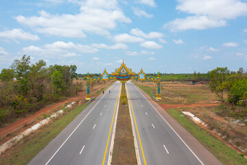 Aerial top view of arch door gate of district with street road with green agricultural fields in countryside or rural area in Asia, Thailand. Nature landscape