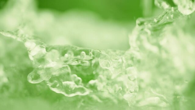 Green liquid in slow motion. Crystal clear water splash. Concept of natural springs and wellness or beauty products. Green tea or aloe vera extract. Cold mineral water in slow motion