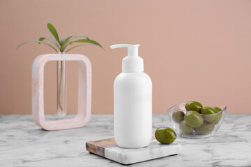 Fototapeta na wymiar Bottle of cosmetic product with olive essential oil on white marble table