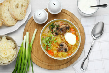 Delicious sauerkraut soup with mushrooms, green onion, dill and sour cream served on white table, flat lay