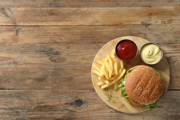 Delicious burger with beef patty, sauce and french fries on wooden table, top view. Space for text