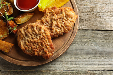 Tasty schnitzels served with potatoes, ketchup and pepper on wooden table, top view. Space for text