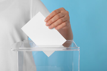 Woman putting her vote into ballot box on light blue background, closeup