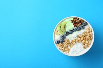 Tasty smoothie bowl with fresh kiwi fruit, blueberries and oatmeal on light blue background, top view. Space for text