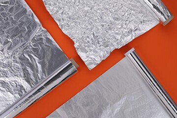 Different rolls of aluminum foil on orange background, flat lay