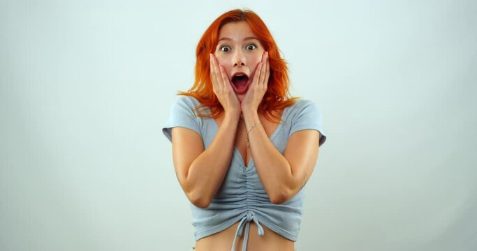 A young girl in a studio environment looks at the camera, puts her hands to her face in slow motion and makes gestures and facial expressions that show that she is surprised