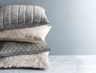 Stack of cushions, sweater pillows on a white marble table with a grey wall background. Copy space