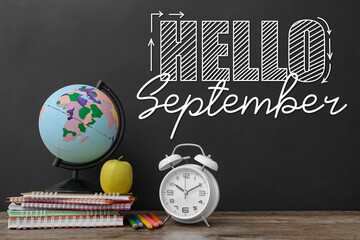 Globe with alarm clock, apple and stationery on table near chalkboard with written text HELLO...