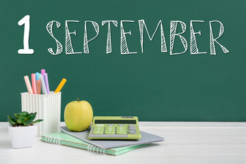 Apple with calculator and stationery on table near chalkboard with written text 1 SEPTEMBER