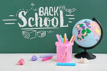 Globe with stationery and crumbled paper on table near chalkboard with written text BACK TO SCHOOL