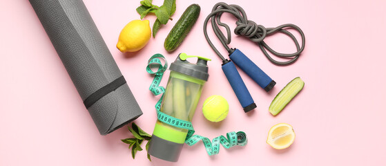 Sports bottle of cucumber lemonade with yoga mat, jumping rope and measuring tape on pink background