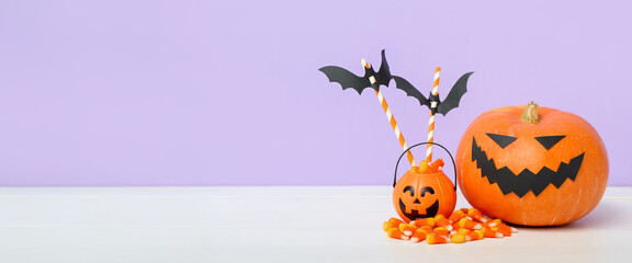 Pumpkins, corn candies and paper bats on table against lilac background with space for text. Halloween banner