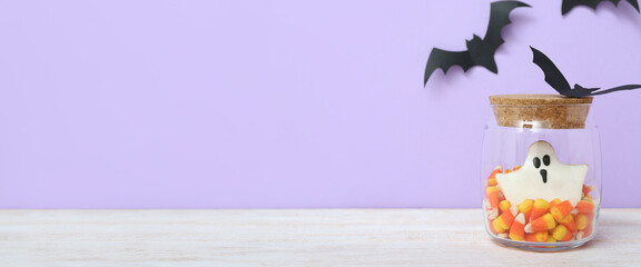 Jar with Halloween sweets and paper bats on lilac background with space for text