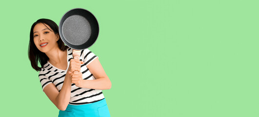 Young Asian woman holding frying pan on green background with space for text