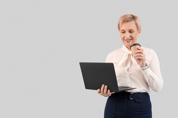 Mature businesswoman with laptop and coffee on grey background