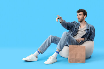 Handsome young man with mobile phone pointing at something on blue background