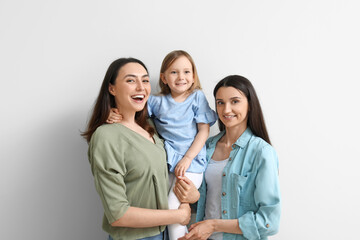 Young lesbian couple with adopted little girl on light background