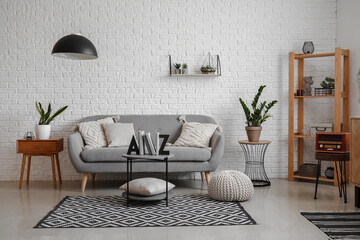 Interior of living room with sofa, houseplants and stylish holder for books on coffee table