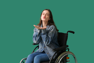 Fototapeta premium Young woman in wheelchair blowing kiss on green background