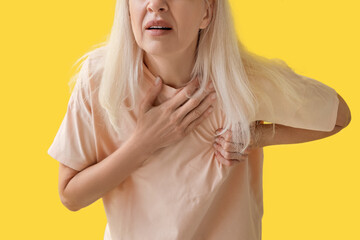Mature woman having heart attack on yellow background, closeup