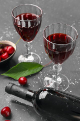 Glasses and bottle of sweet cherry liqueur with berries on grey grunge background