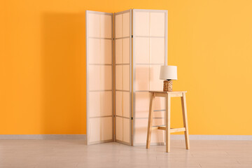Folding screen, table and lamp near orange wall