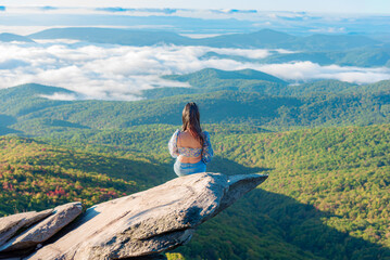 Woman sits on the cliff at Rough Ridge Lookout , Blue Ridge Parkway near Grandfather Mountain in fall season.