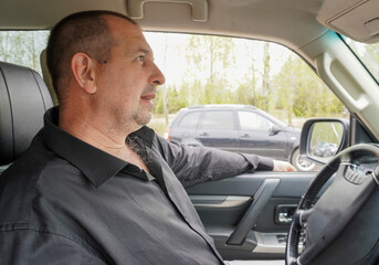 Man 50 years old in a black shirt driving a car