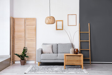 Interior of light living room with grey sofa and branches in vase on wooden table
