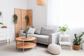Interior of light living room with grey sofa, wooden coffee table and houseplants