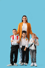 Fototapeta premium Young female teacher with three diverse schoolboys wearing backpacks, education and learning concept, isolated on blue background