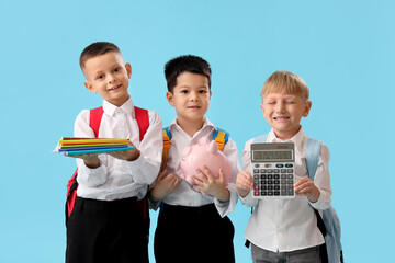 Little school boys with stationery and piggy bank on light blue background
