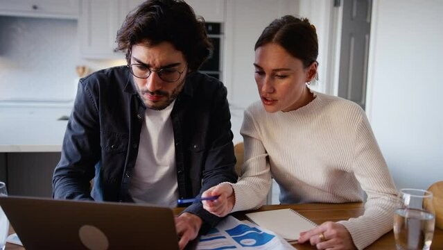 Worried young couple at home looking at laptop in kitchen counter worried about bills and cost of living crisis working out budget- shot in slow motion
