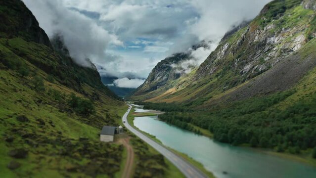 A road winds along the river through the green Norwegian valley. Aerial view, pan forward.