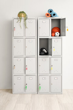 Modern locker with sports equipment and plant near light wall