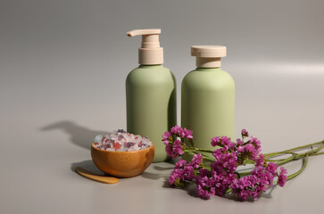 Fototapeta na wymiar Bottles of cosmetic products with beautiful flowers and sea salt on grey background