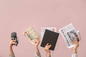 Female hands with different newspapers, notebook and microphone on color background