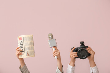 Female hands with newspaper, microphone and photo camera on color background