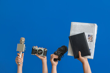Female hands with microphones, photo camera, notebook and newspaper on blue background