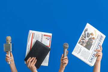 Female hands with newspapers, microphones and notebook on blue background