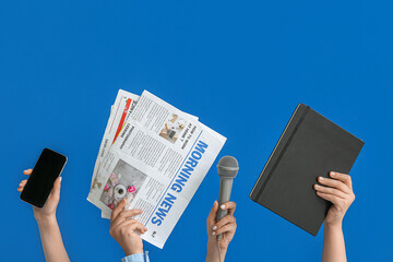 Female hands with mobile phone, newspapers, microphone and notebook on blue background
