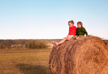 Naklejka na ściany i meble Two little children are sitting on a haystack in a field at sunset