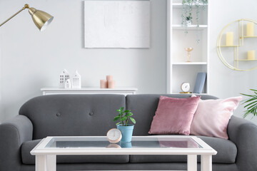 Interior of light living room with grey sofa and glass coffee table