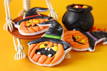 Naklejka premium Skeleton with tasty cookies in shape of pumpkin for Halloween celebration on orange background, closeup