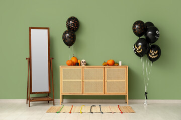Different black Halloween balloons, chest of drawers, pumpkins and mirror near green wall in room